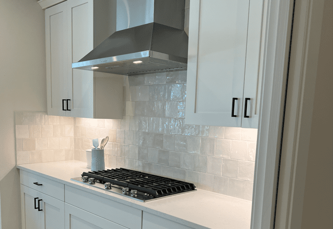 A kitchen with white cabinets, white tile and a gas cooktop.