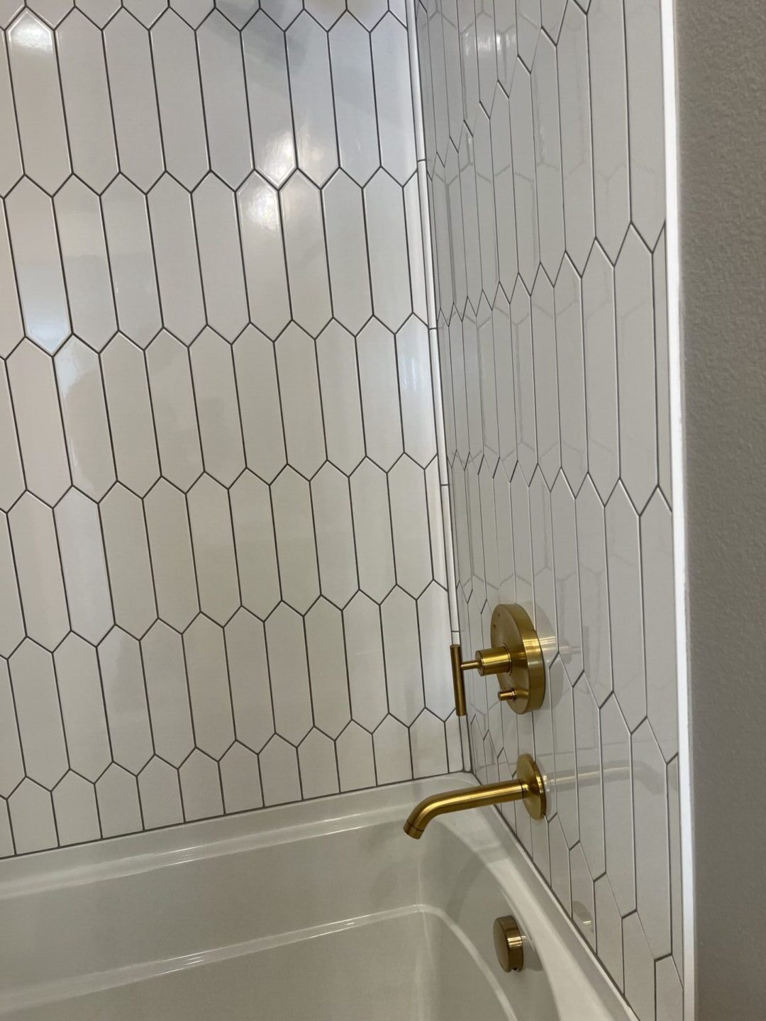 A bathroom with white tile and gold fixtures.