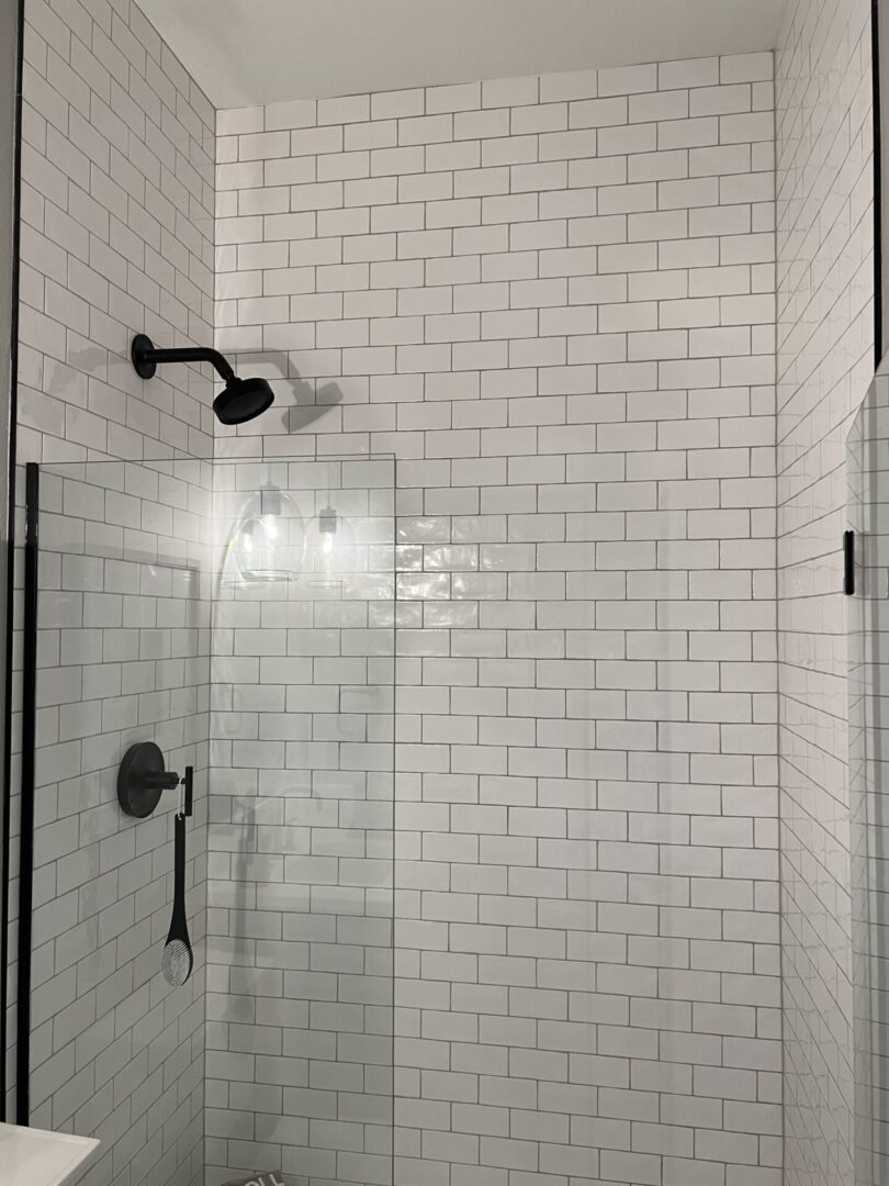 A shower with white tile and black fixtures.