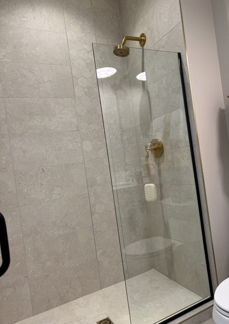 A shower with glass doors and a gold handle.