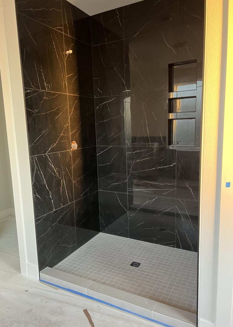 A black marble shower with a white floor and walls.