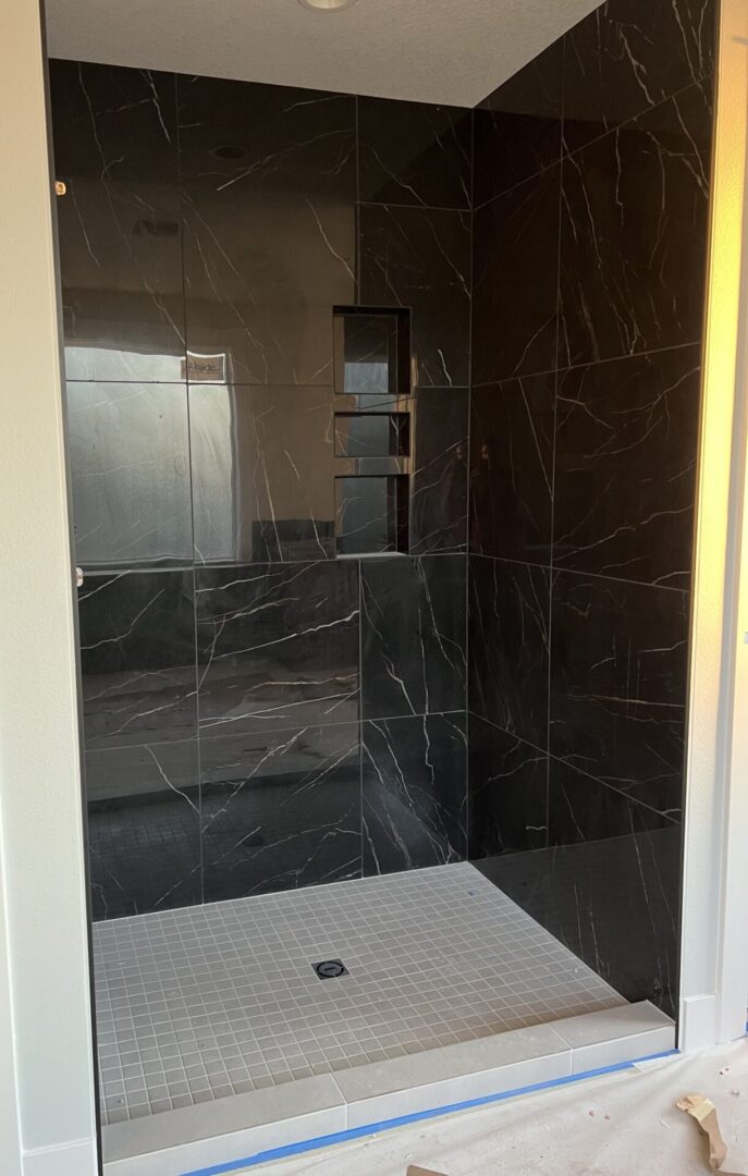 A black tiled shower with white tile floor.