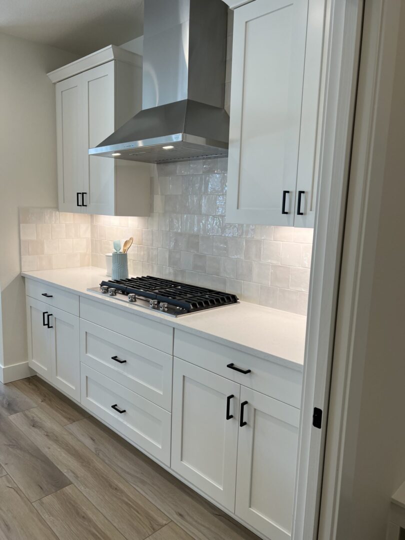 A kitchen with white cabinets, white tile and a gas cooktop.